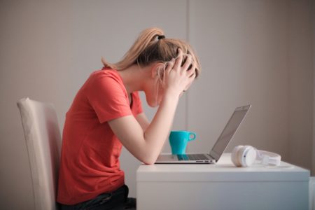 woman holding her head looking at her laptop