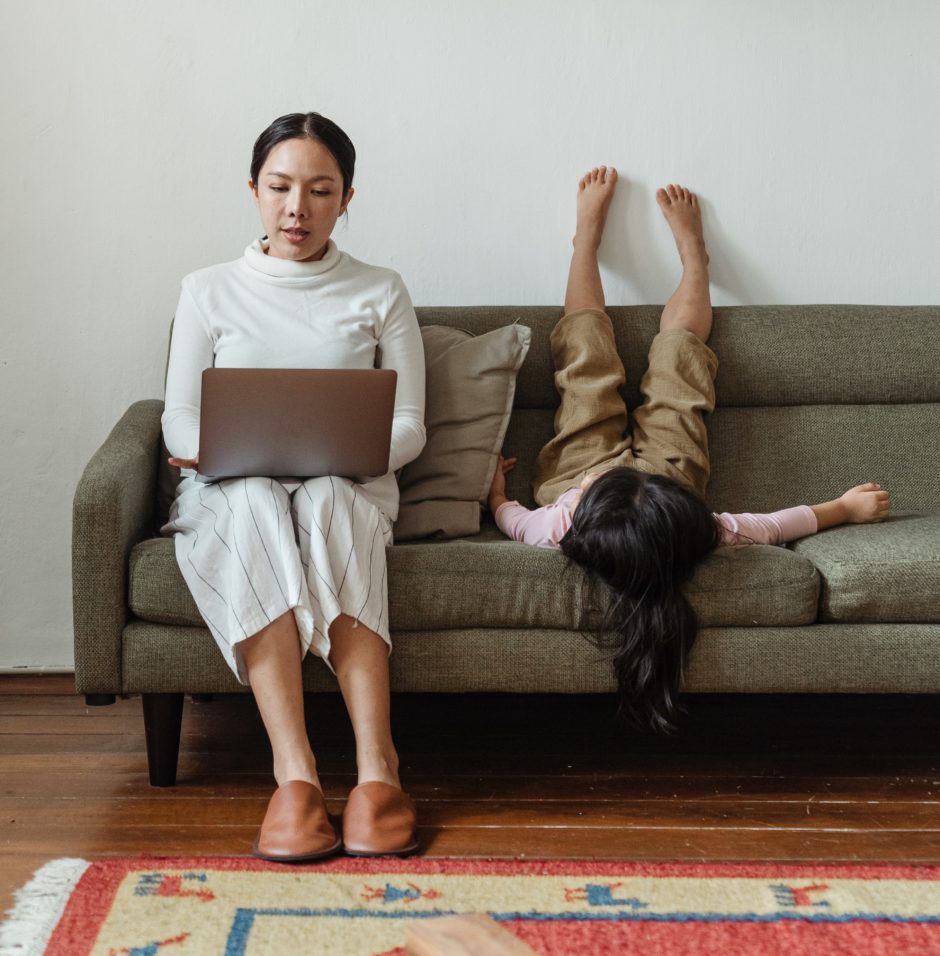 focused mother working on laptop near daughter on couch