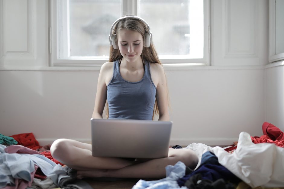 woman sitting cross-legged and listening to headphones while typing on a laptop