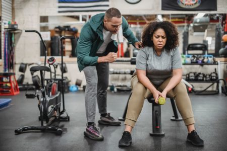 a man who is a personal trainer encourages a woman sitting on a bench in a gym